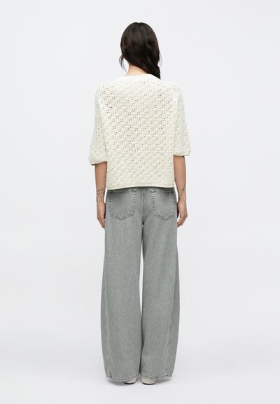 Κρεμ πλεκτό τοπ με κοντά μανίκια και ανοιχτό πλεκτό σχέδιο, σε συνδυασμό με ανοιχτό γκρι τζιν παντελόνι με φαρδιά πόδια, πίσω τσέπες και ψηλή μέση.