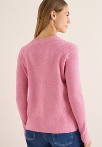 Różowy sweter z prążkowanej dzianiny z dekoltem w kształcie litery V i długimi rękawami, o dopasowanym kroju i miękkiej fakturze, zestawiony z niebieskimi dżinsami.