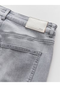 Gros plan d'un jean en denim gris clair montrant une poche arrière et une étiquette de marque en cuir blanc cousue près de la ceinture.
