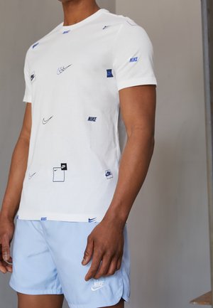Hvid bomuld T-shirt med forskellige blå Nike-logoer; kombineret med lyseblå shorts, begge understreger en afslappet atletisk stil.