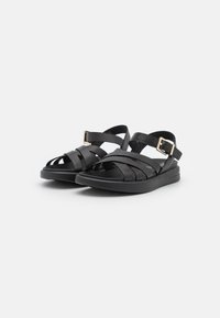 Sandali neri con un design a strappo, realizzati in materiale gommoso. Presentano una fibbia regolabile e una suola imbottita per il comfort.