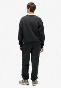Mørkegrå bomulds-sweatshirt og matchende bukser, der har en løs pasform og ribbede manchetter. Skoene er lysegrå med mørke detaljer.