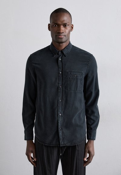 Chemise noire à manches longues en tissu doux, avec une poche poitrine et un ourlet arrondi. Dotée de boutons contrastants et d'une texture mate.