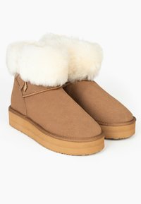 Botines de ante en color marrón claro con un lujoso puño de piel sintética blanca y suela de goma plana; presenta una costura a lo largo del borde del empeine y una etiqueta en el lateral.