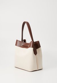 Borsa a tracolla in tela beige con forma strutturata, dettagli in pelle marrone, una maniglia corta e un nastro decorativo nella parte superiore.