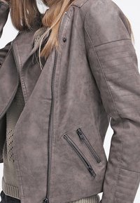 Grau faux Lederjacke im Bikerdesign, mit einem diagonalen Frontreißverschluss, gesteppten Schulterakzenten und zwei Reißverschlusstaschen.