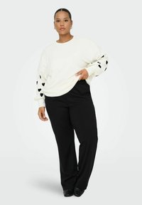 Sweatshirt blanc avec des motifs de cœurs noirs sur les manches, assorti à un pantalon noir. Texture lisse, coupe décontractée et design minimaliste.