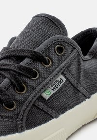 Ciemnoszare płócienne sneakersy z okrągłymi metalowymi oczkami, czarnymi sznurowadłami i białą gumową podeszwą, z zieloną etykietą z napisem "natural world".