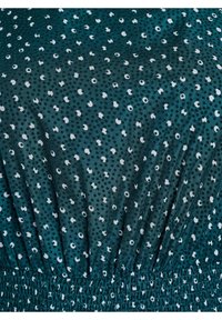 Tirkizni materijal s uzorkom razbacanih bijelih i tamnozelenih točkica, s gumiranim elastičnim rubom i glatkom teksturom.