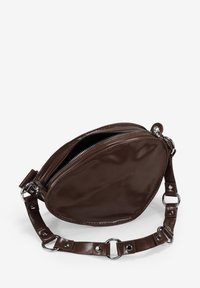 Bolso de cuero marrón con forma redondeada, que cuenta con un cierre de cremallera y una correa de cadena con acentos plateados. Textura lisa y diseño minimalista.