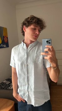 Hellblau und weiß gestreiftes kurzärmeliges Hemd mit Knopfleiste aus Stoff, mit spitzem Kragen und Brusttasche, getragen mit dunklen Jeans.
