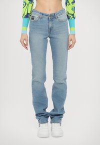 Svetlo modri denim jeans s ravnim krojem, zasnovo s petimi žepi in subtilno teksturo. Nosi se z belimi športnimi čevlji za kontrast.