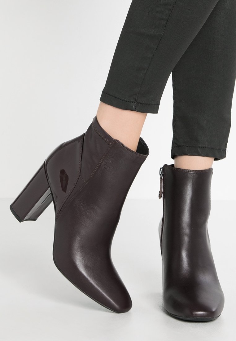 Ciemnobrązowe skórzane botki za kostkę z ostrym noskiem i masywnym, wysokim obcasem. Posiadają boczny zamek błyskawiczny oraz błyszczący akcent na jednej z botków.