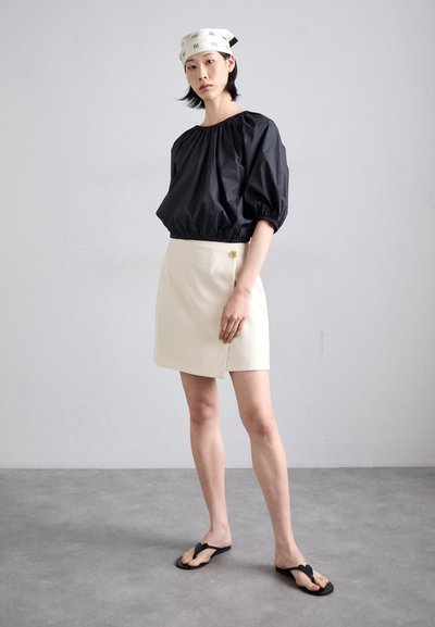 Black puff-sleeve top, white wrap skirt with button detail, and black flip-flops on a model against a neutral background.