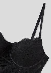 Reggiseno in pizzo nero con motivi floreali, coppe sagomate e spalline regolabili. Texture morbida con sottoseno liscio e chiusura a gancetto.