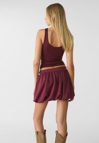 Burgundy linne och matchande elastisk midja ballongkjol, som visar en slät textur, med ljusbruna cowboystövlar.