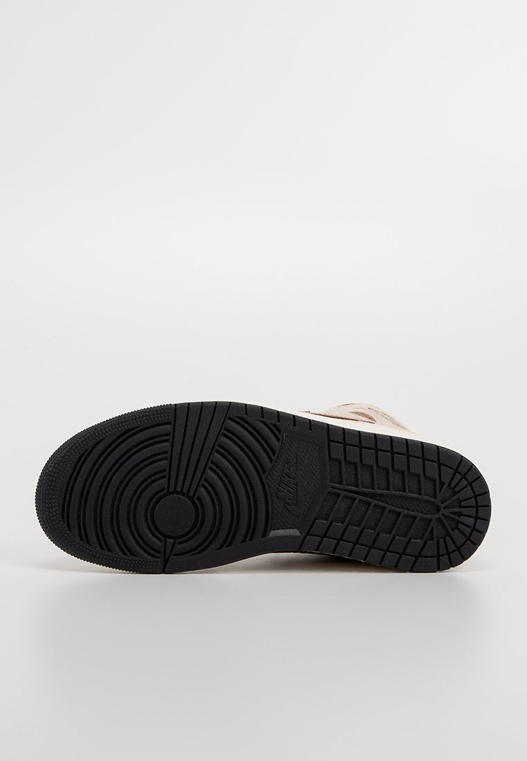 Suela de zapatilla Nike con una suela exterior de goma negra texturizada, que presenta patrones circulares y lineales, y una parte superior de color crema para contraste.
