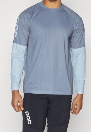 Homme portant un haut de sport bleu et bleu clair à manches longues et un pantalon noir avec le logo blanc "POC" sur la cuisse gauche et la manche droite.