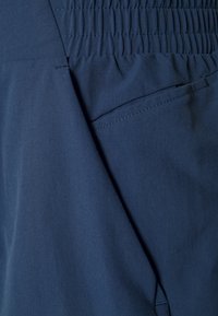 Námořnická modrá tkanina s jemnou texturou, vybavená elastickým pasem a diskrétními bočními kapsami. Zaměření na funkční designové detaily.