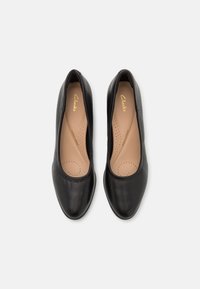 Ballerine in pelle nera con una texture liscia, punta arrotondata e bordo elasticizzato. Soletta imbottita di un leggero color tan con dettagli perforati.