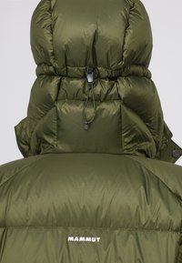 Giacca a vento verde con collo alto e cappuccio oversize. Presenta una chiusura con cordino e un piccolo logo bianco sulla parte posteriore.