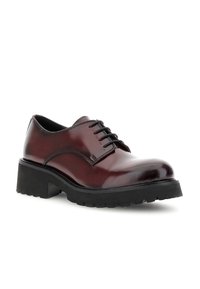 Scarpa stringata in pelle lucidada bordeaux con suola nera a carrarmato spessa e tacco basso, inclinata a sinistra su uno sfondo bianco.