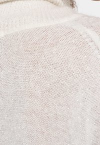 Maglione a maglia di un leggero beige con una finitura morbida e testurizzata. Presenta sottili filamenti luccicanti, un collo alto e bordi a coste.