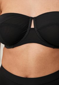 Zwarte strapless beha met een gladde textuur, gebogen cups en een sluiting aan de voorkant. Het ontwerp biedt minimale bedekking en ondersteuning.