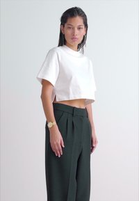 T-shirt court blanc à manches courtes, associé à un pantalon tailleur taille haute de couleur vert foncé. Présente une coupe élégante et un tissu lisse.