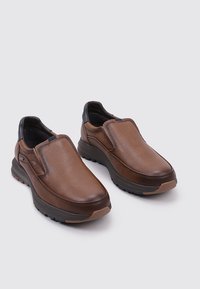 Zapatos loafers de cuero marrón con una textura suave, suela acolchada y un acento negro en el talón. Diseño de punta redonda.