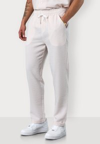 Helle, strukturierte Hose mit Karomuster, elastischem Bund und Kordelzug. Kombiniert mit weißen Sneakers für einen lässigen Look.