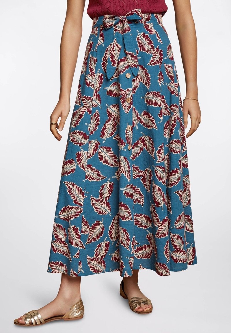 Maxi-Rock aus blauer Stoff mit einem Blätterdruck in Burgund und Creme. Mit gebundenem Taillenbund und Knopfverschluss, kombiniert mit goldenen Sandalen.