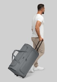 Grau gerollte Reisetasche mit zwei schwarzen Rädern, einem ausziehbaren Griff und zwei seitlichen Tragegurten; verfügt über eine glatte Stoffoberfläche.