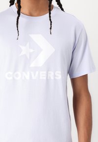 Svetložlté tričko s krátkym rukávom, na ktorom sa nachádza veľké biele logo Converse, hviezda a dizajn šípky na prednej strane. Vyrobené z mäkkej bavlny.