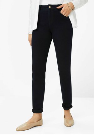 Navyblaue Skinny-Jeans mit hoher Taille, ausgestattet mit Fronttaschen, einem einzigen Knopfverschluss und umgeschlagenen Säumen, kombiniert mit beigen Ballerinas.