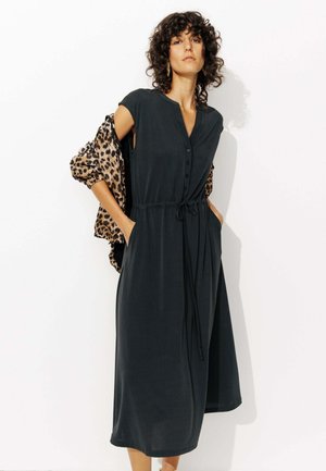 Robe maxi sans manches vert foncé avec un devant à boutons, une taille cintrée à nouer et des poches sur les côtés, accompagnée d'un châle à motif léopard.