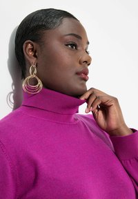 Magenta Rollkragenpullover mit geripptem Kragen und Bündchen; Modell trägt goldene Creolen. Glatte Textur mit leichtem Glanz.