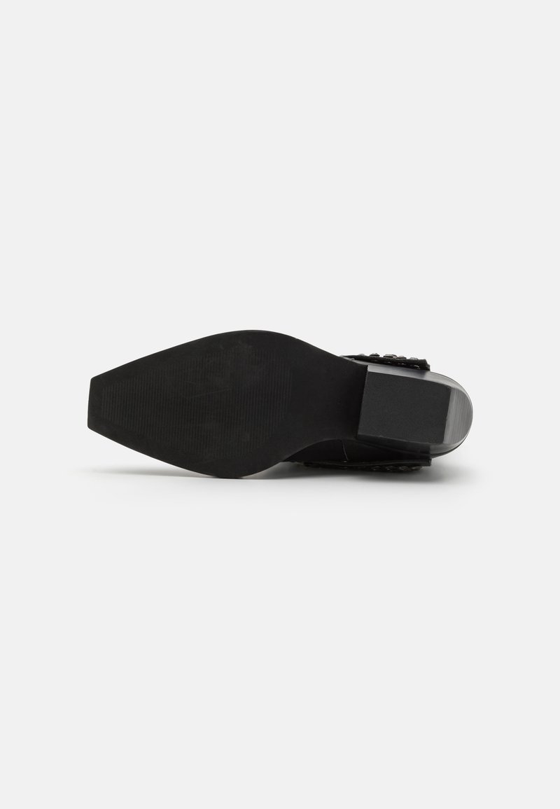 Sandalia de tacón negro con suela texturizada, diseño de tiras anchas y tacón bajo. Acabados en cuero suave en la tira.