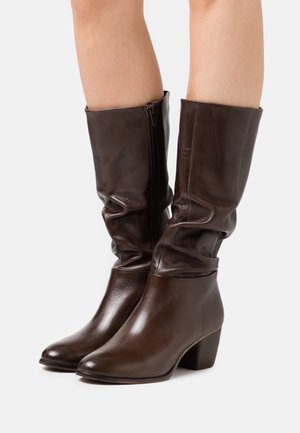 Bottes en cuir marron montant jusqu'au genou avec un design décontracté, bout arrondi et talon épais. Elles comportent une fermeture éclair latérale et une texture lisse et brillante.
