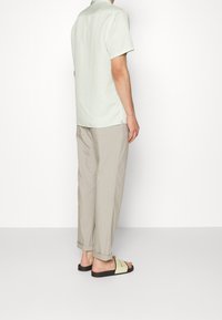 Camicia verde chiaro a maniche corte con un motivo sottile, abbinata a pantaloni beige svasati e sandali neri con una fascia verde chiaro.