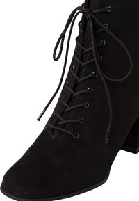 Bottine en daim noir avec talon bloc, bout pointu, et fermeture à lacets noirs avec œillets métalliques.