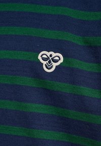 Marinblå och grönrandig tyg med en texturerad yta; har en vit broderad bi-logotyp på vänster sida.