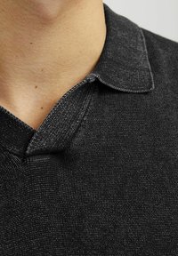 Chemise polo noire en tricot textur�é, avec un col court et structuré et des détails de coutures visibles le long des bords.