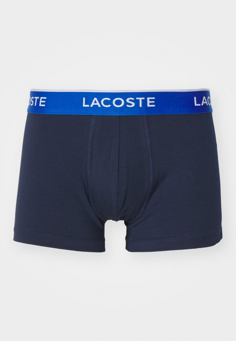 Boxers pour hommes bleu marine avec ceinture élastique présentant une bande bleue portant l'inscription "LACOSTE." Tissu doux avec une coupe ajustée et sans motifs.