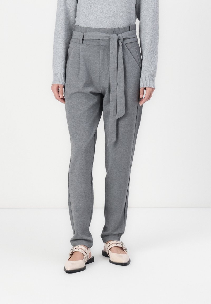 Personne portant un pantalon gris sur mesure avec une ceinture en tissu et des chaussures plates rose pâle avec double bride et petites boucles.