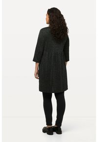 Tunique noire texturée avec une taille froncée et des manches trois-quarts, associée à des leggings noirs et des chaussures à plateforme, vue de dos.