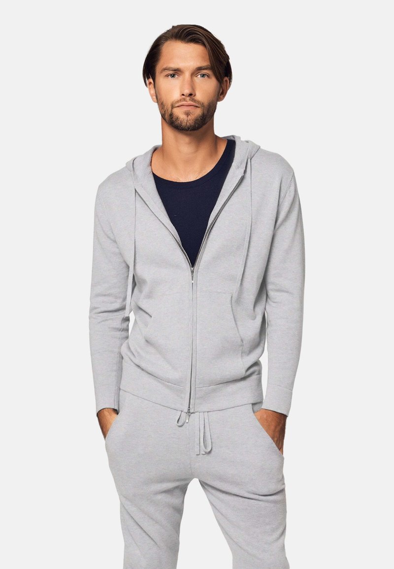 Felpa grigia chiara con zip, dotata di cordino e tasche frontali, abbinata a una maglietta a girocollo blu navy. Tessuto morbido e vestibilità casual.