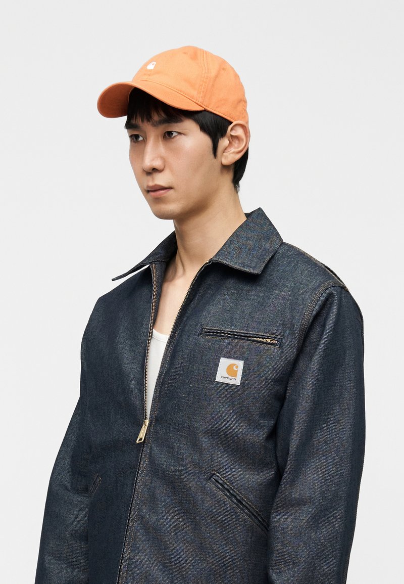 Veste en jean foncé avec fermeture éclair à l'avant et grand col, ornée d'un écusson logo carré. Assortie à une casquette en coton orange.