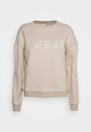 Felpa beige realizzata in morbido tessuto, con collo tondo, spalle scese e logo "GUESS" in lettere lucide sulla parte anteriore.