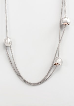 Collier à double chaîne couleur argent avec trois perles métalliques brillantes de forme irrégulière espacées le long des brins sur fond blanc.